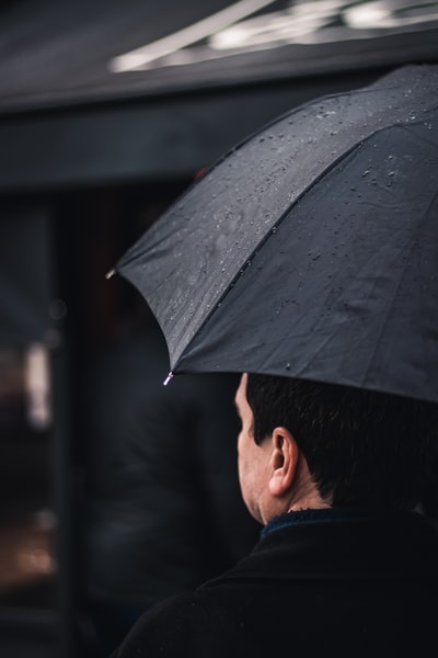 一名身穿黑色上衣、手持黑色雨伞的男子在黑色雨篷附近行走